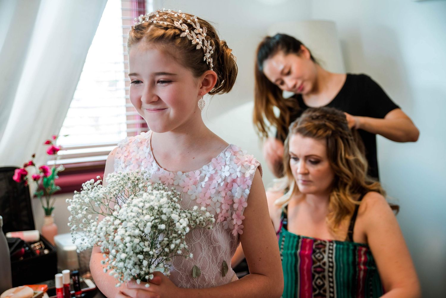 A bride in a lace dress holds baby's breath bouquet while getting ready with her bridal party.