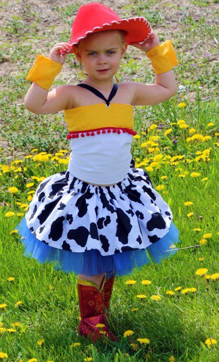 Child in cowgirl costume with red hat and cow print dress posing in field of dandelions.