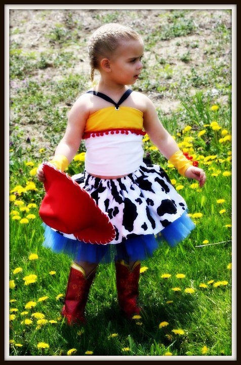 Child wearing colorful cowgirl costume with cow print skirt standing in field of yellow flowers.
