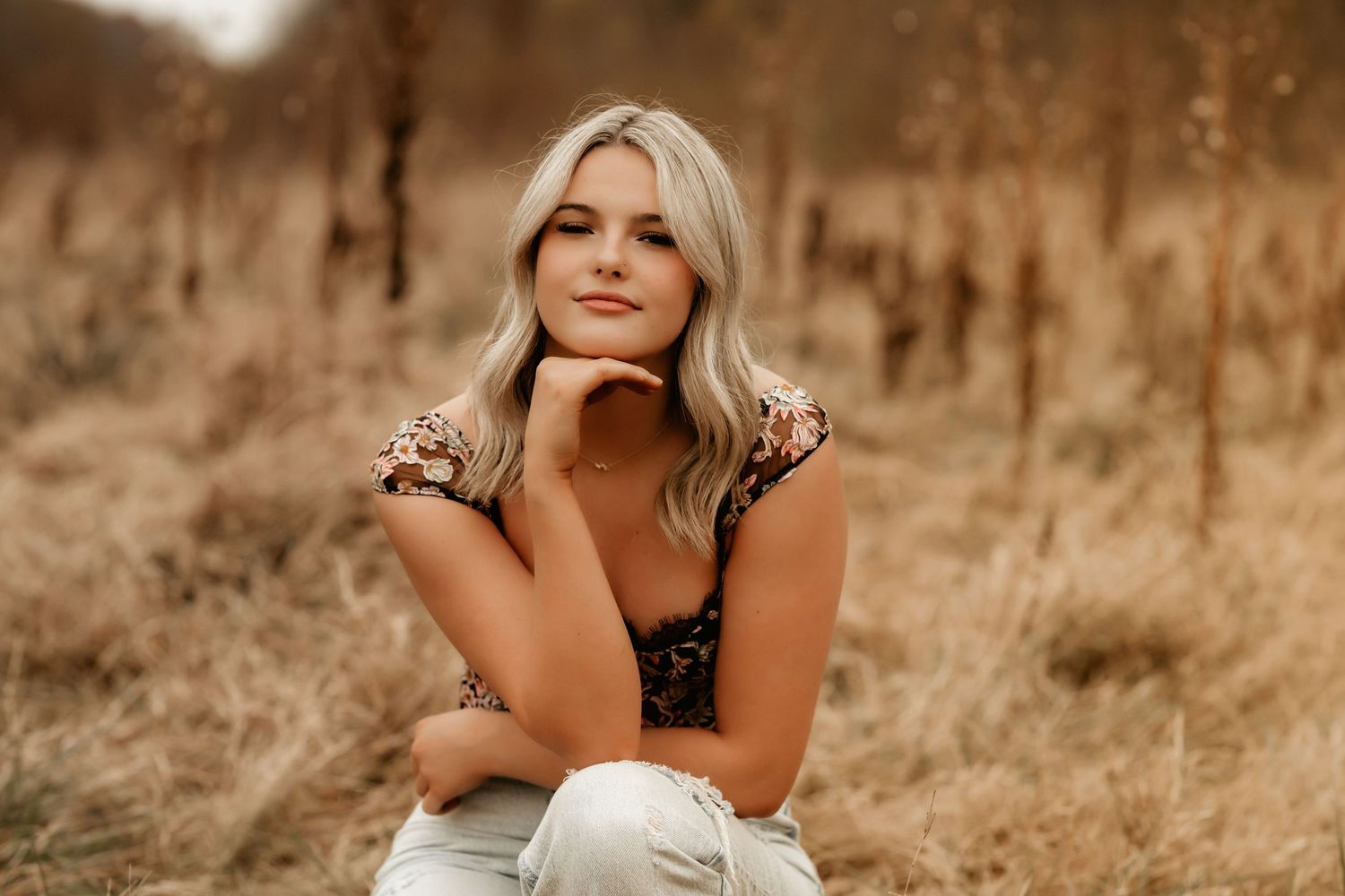 Senior in a field, showcasing a soft smile and accomplishment.
