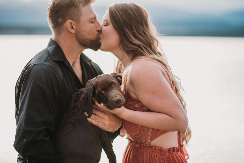 couple kissing with a puppy between them looking at the camera