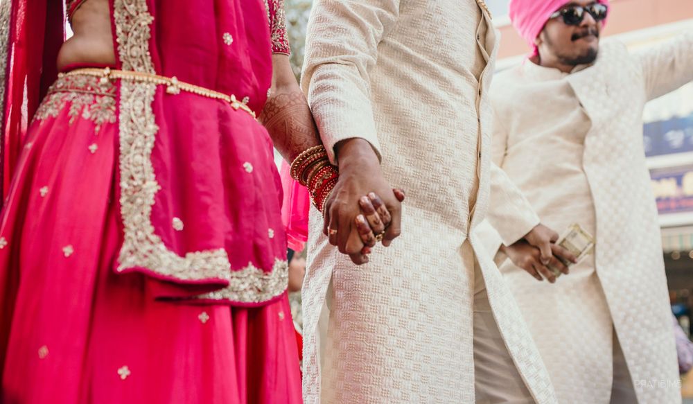 Couple in traditional Indian wedding attire holding hands during ceremony.