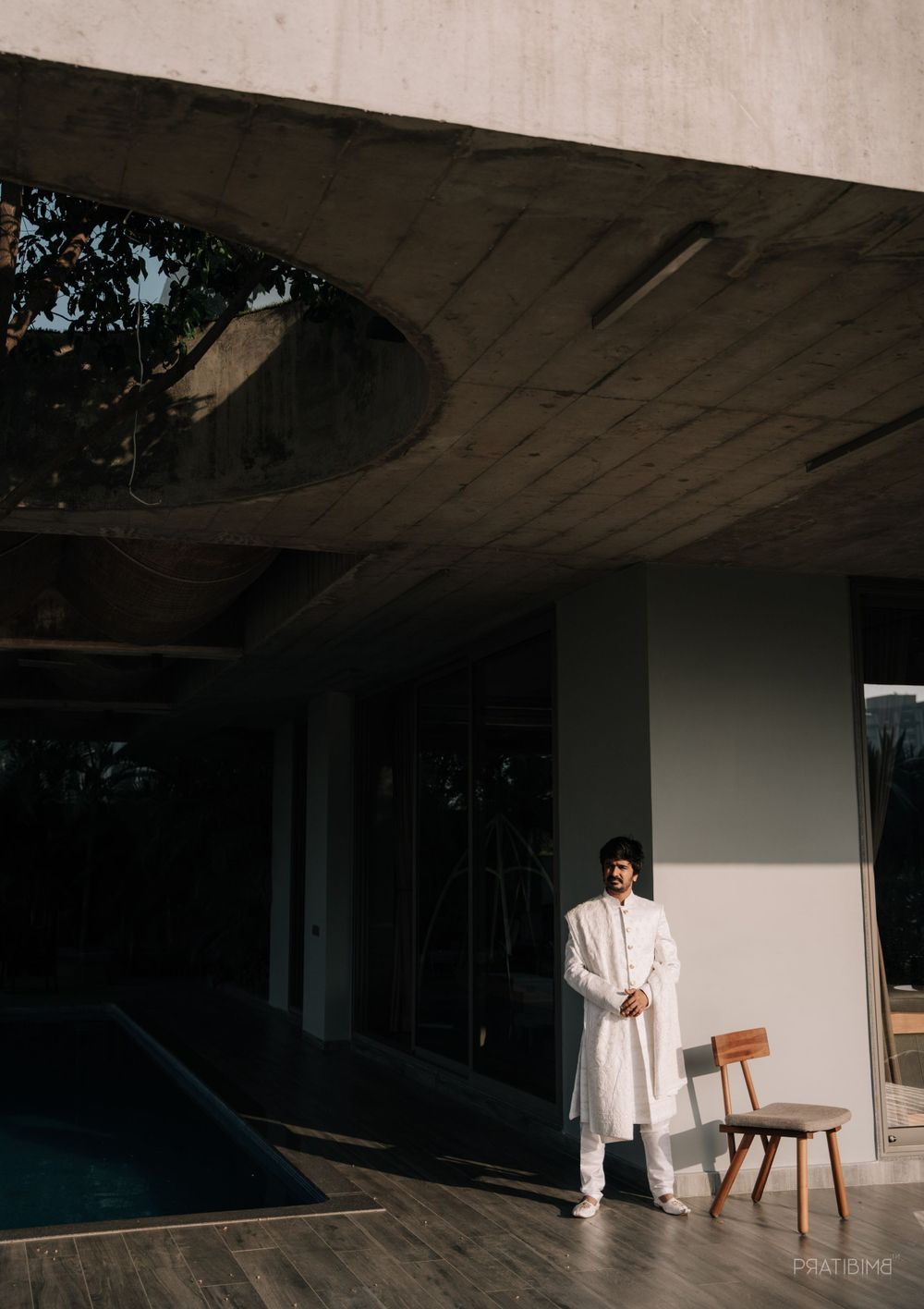 Person in white traditional Indian attire standing near modern architecture and pool.