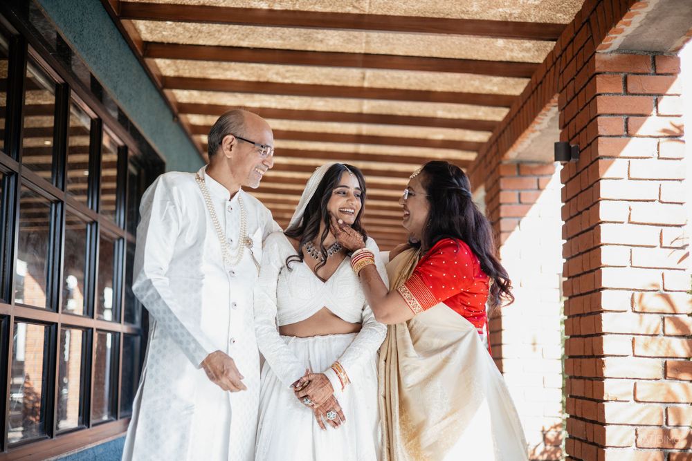 Three people in elegant white traditional attire converse in a hallway with brick walls.