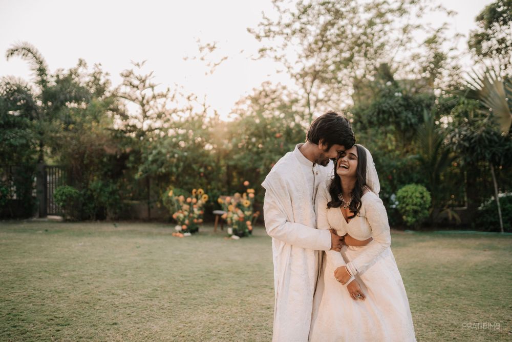 Couple in white traditional attire sharing intimate moment in garden during sunset.