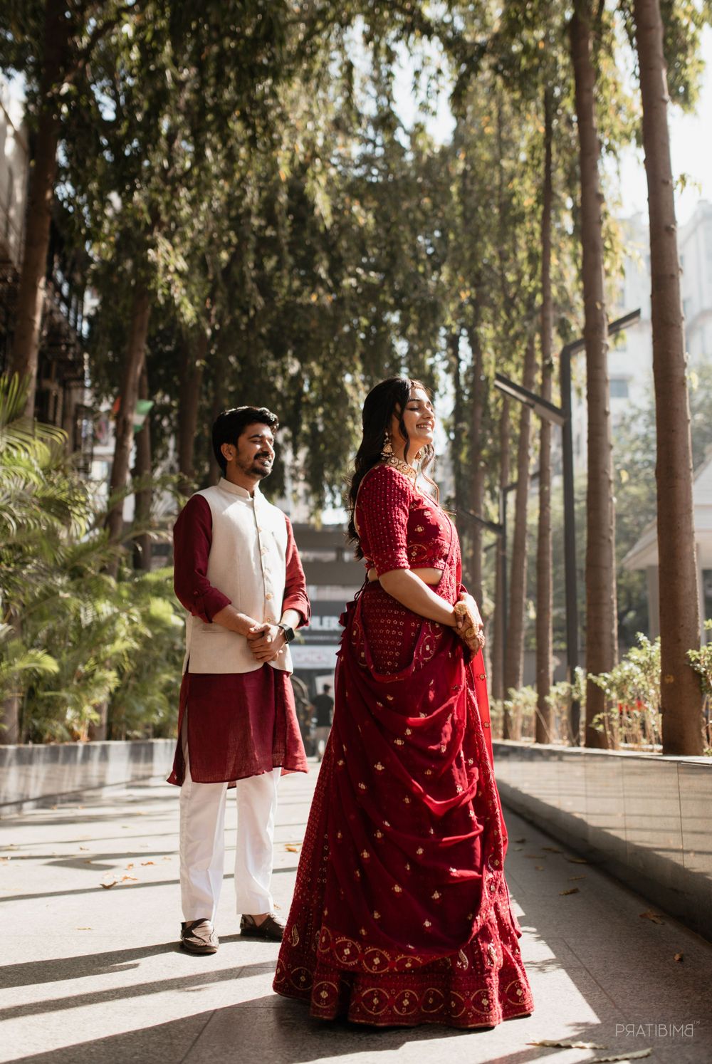 Couple in traditional Indian wedding attire posing in a tree-lined pathway.