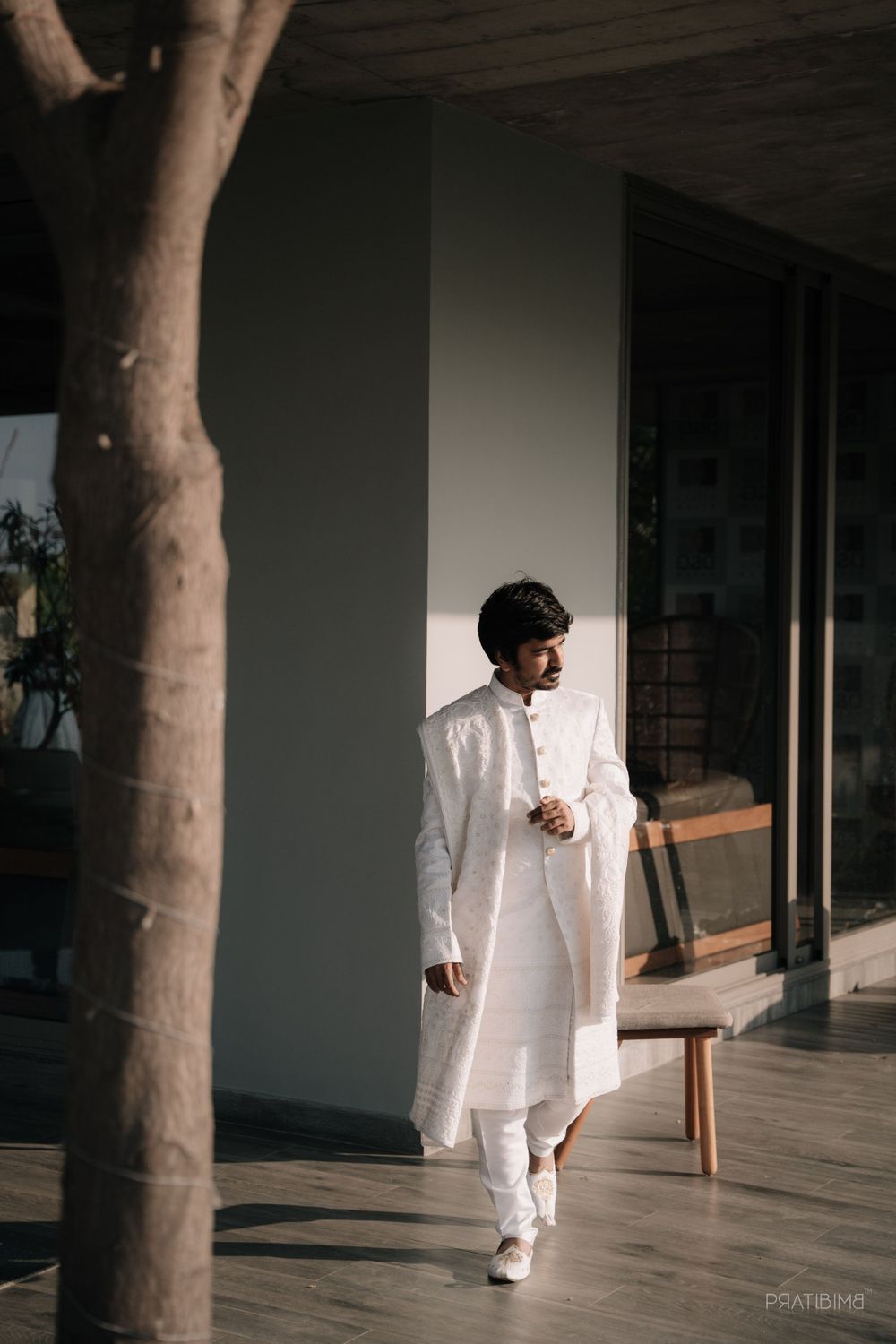 Person in white traditional Indian attire walking on modern patio with dramatic lighting.