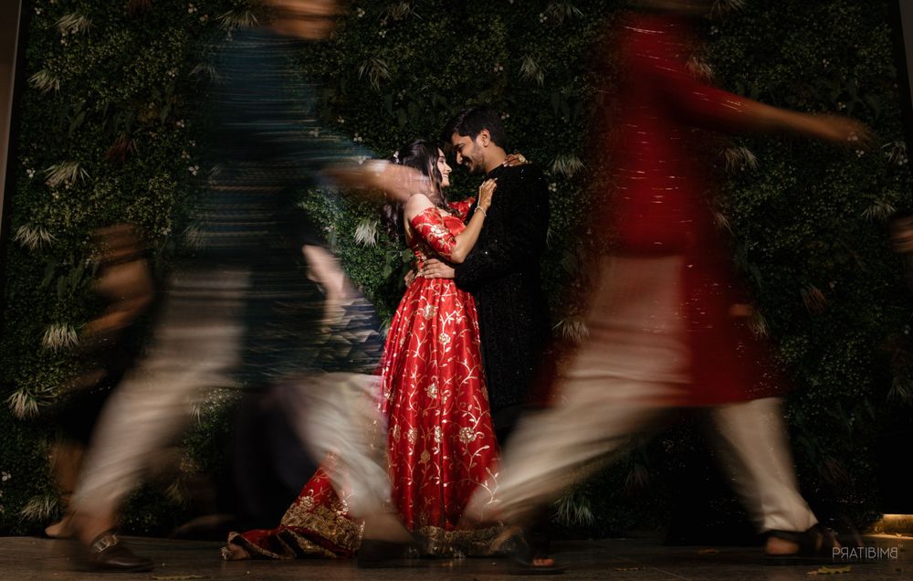 Artistic motion blur photograph of couple dancing in red attire with people walking past.