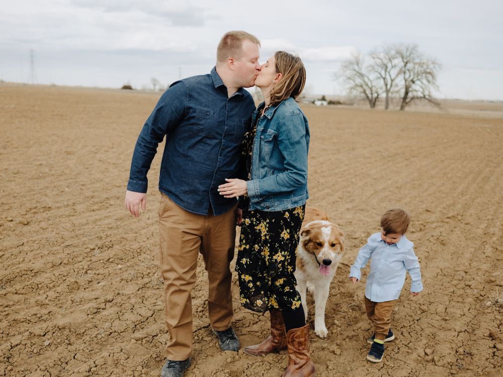 Family and their golden retriever share a sweet moment while walking through a rural field.