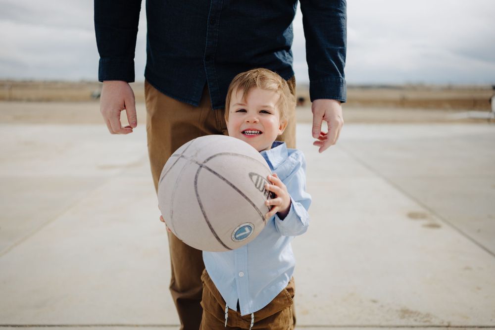 A small child holds a basketball while standing next to an adult on a concrete path.