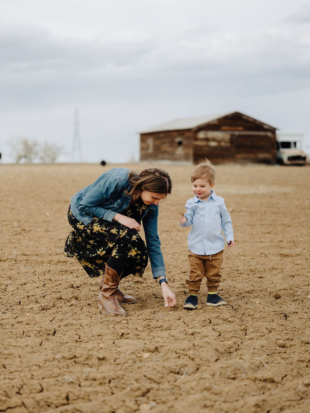 A tender moment captured in a barren field with a rustic barn in the background.