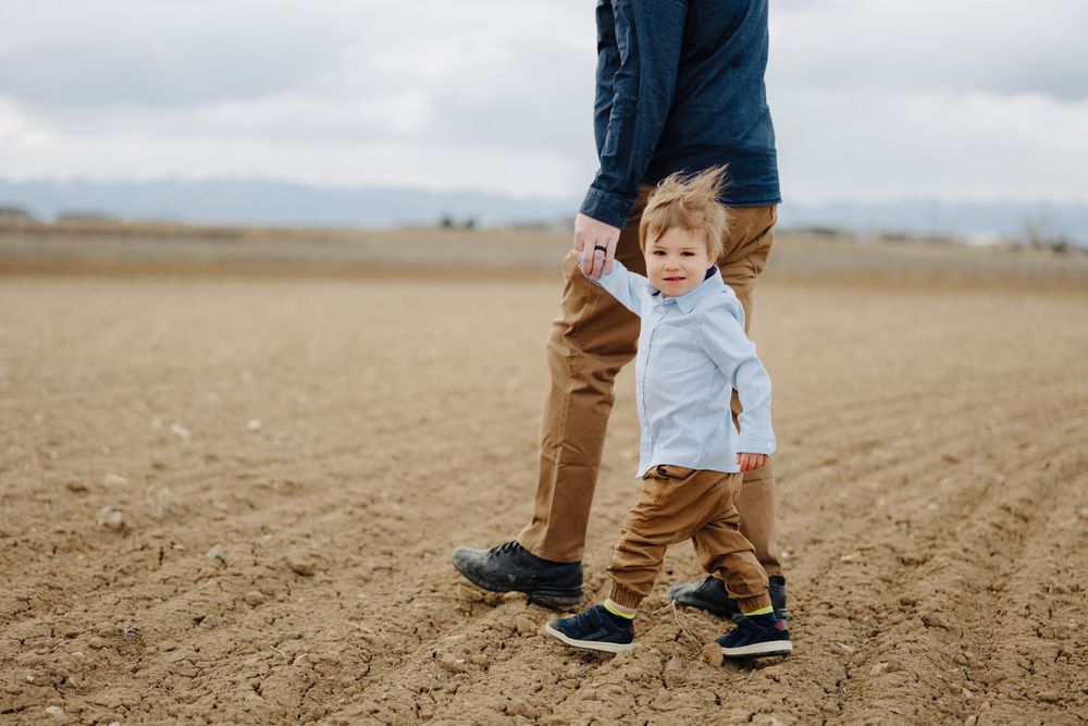 Adult and child walking together in an open field with mountains in the distance.