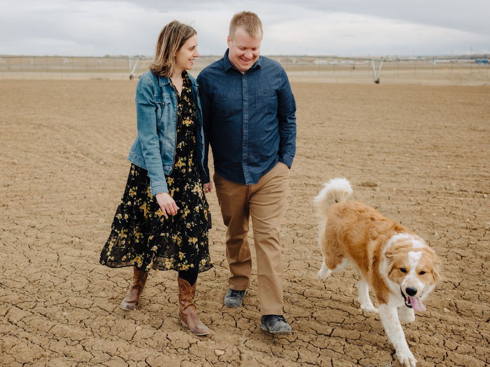 A couple and their golden retriever enjoy a walk through an open field on an overcast day.