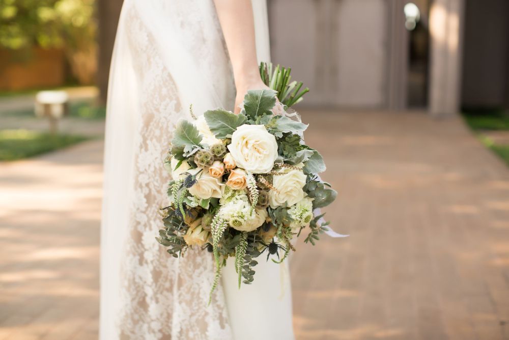 Bridal bouquet of cream roses and greenery held against white lace.