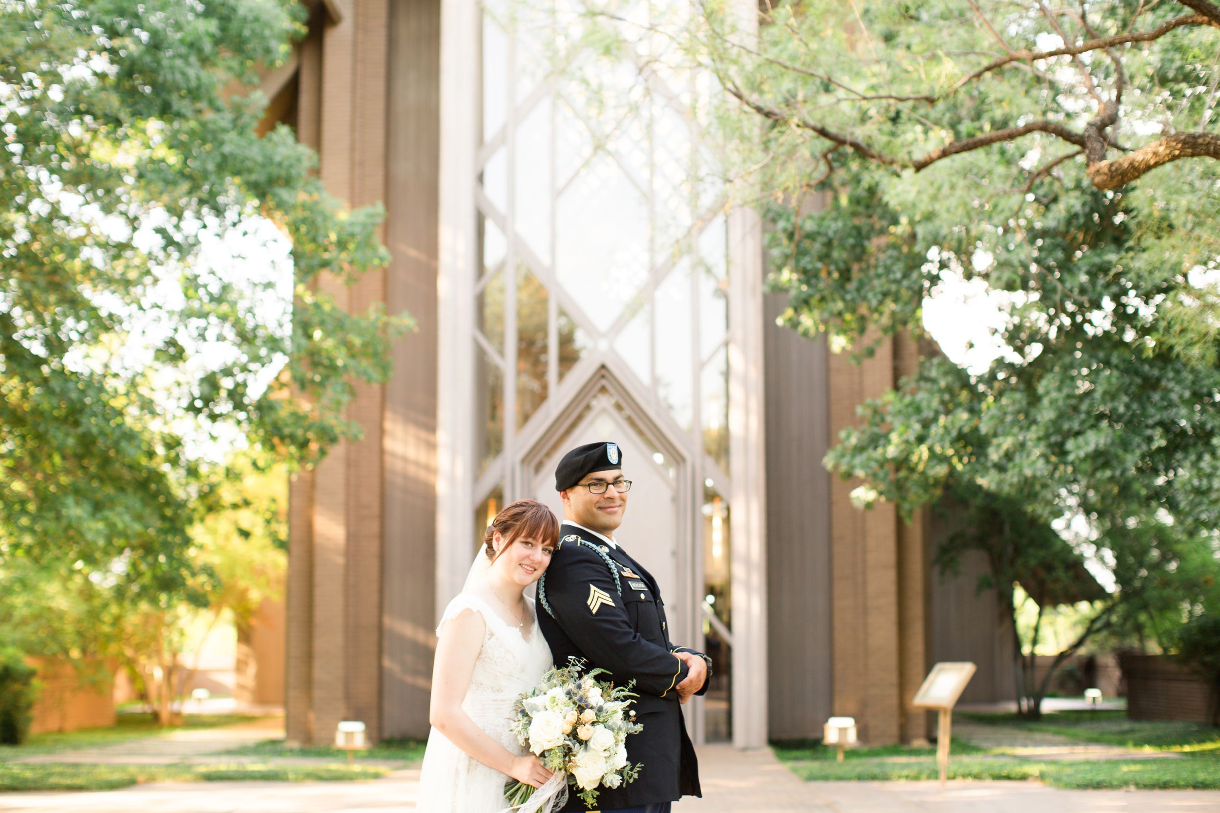 Couple in wedding attire standing beneath gothic church arches at sunset.