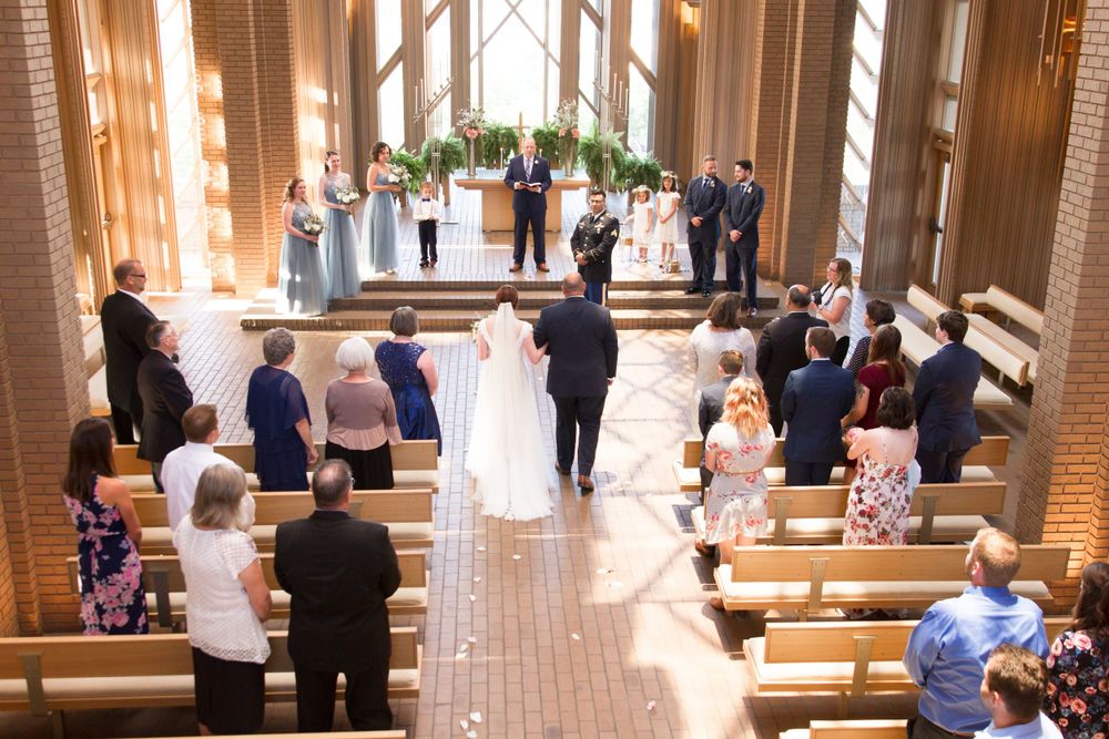 Wedding ceremony in progress inside a beautiful chapel with wooden pews and natural light.