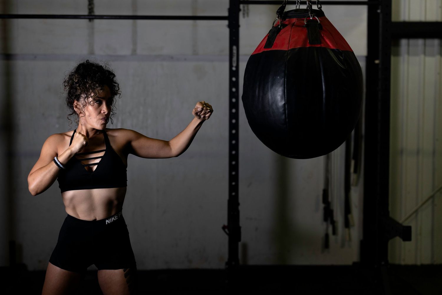 Person in athletic wear throwing punches near a heavy bag during boxing training.