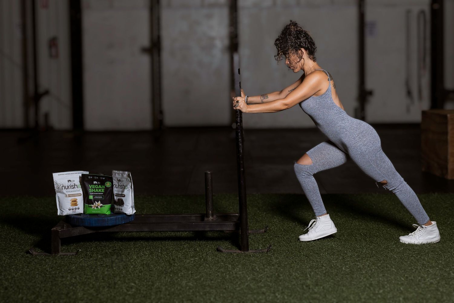 Person in grey workout clothes pushing exercise equipment on artificial turf.