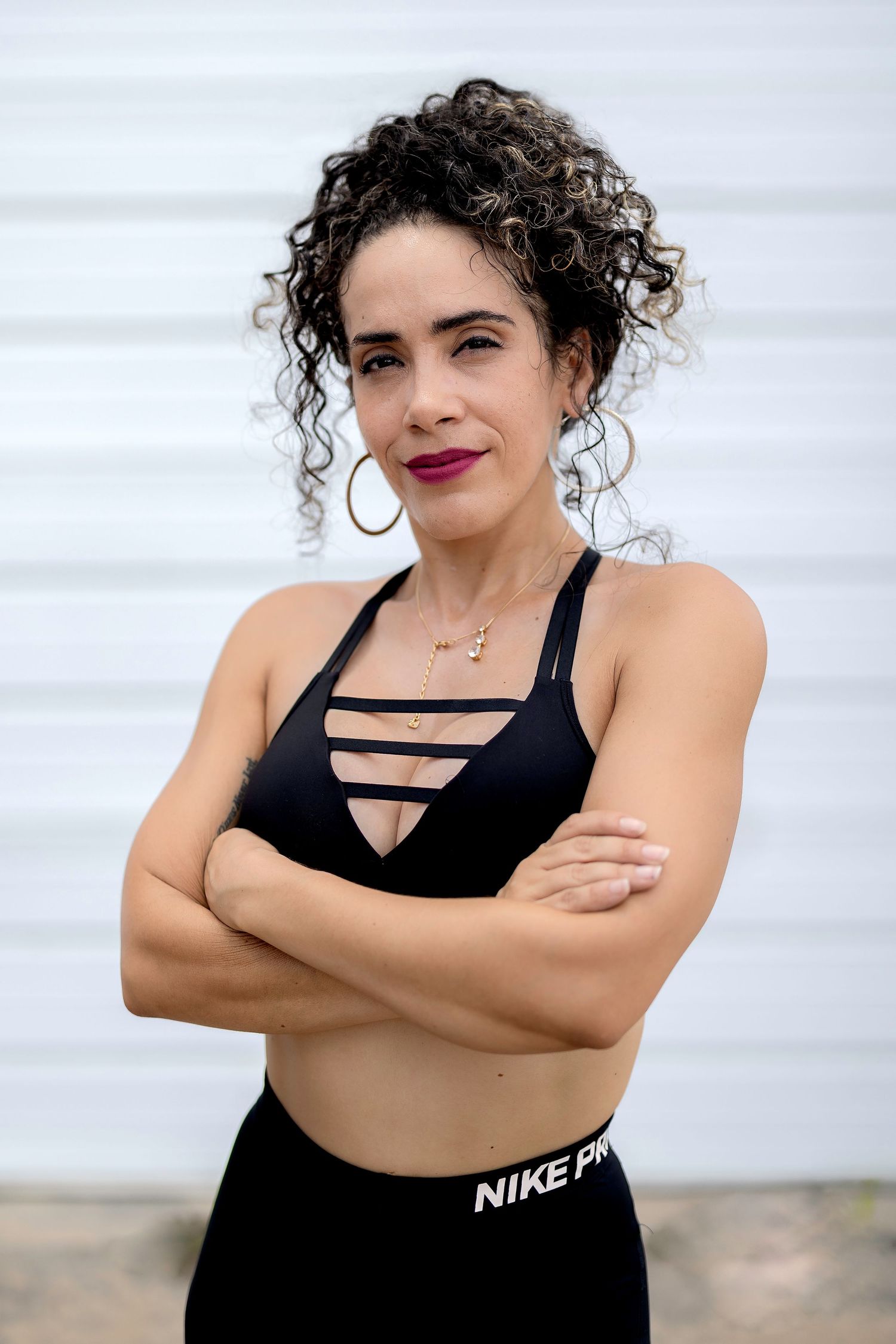 Person in black sports bra with curly hair poses confidently against white background.