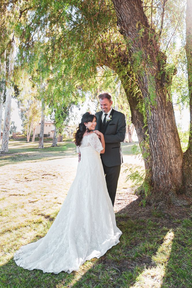 Romantic wedding photos under trees with flowing white lace dress train.