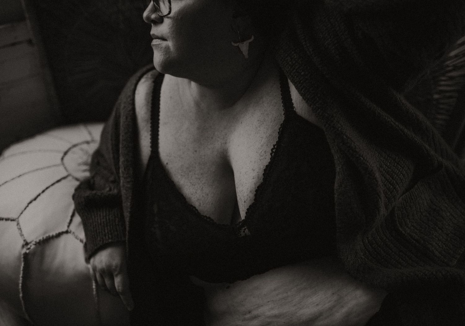 Artistic black and white photograph showing a close-up of a woman in a black bralette against a shadowy background.