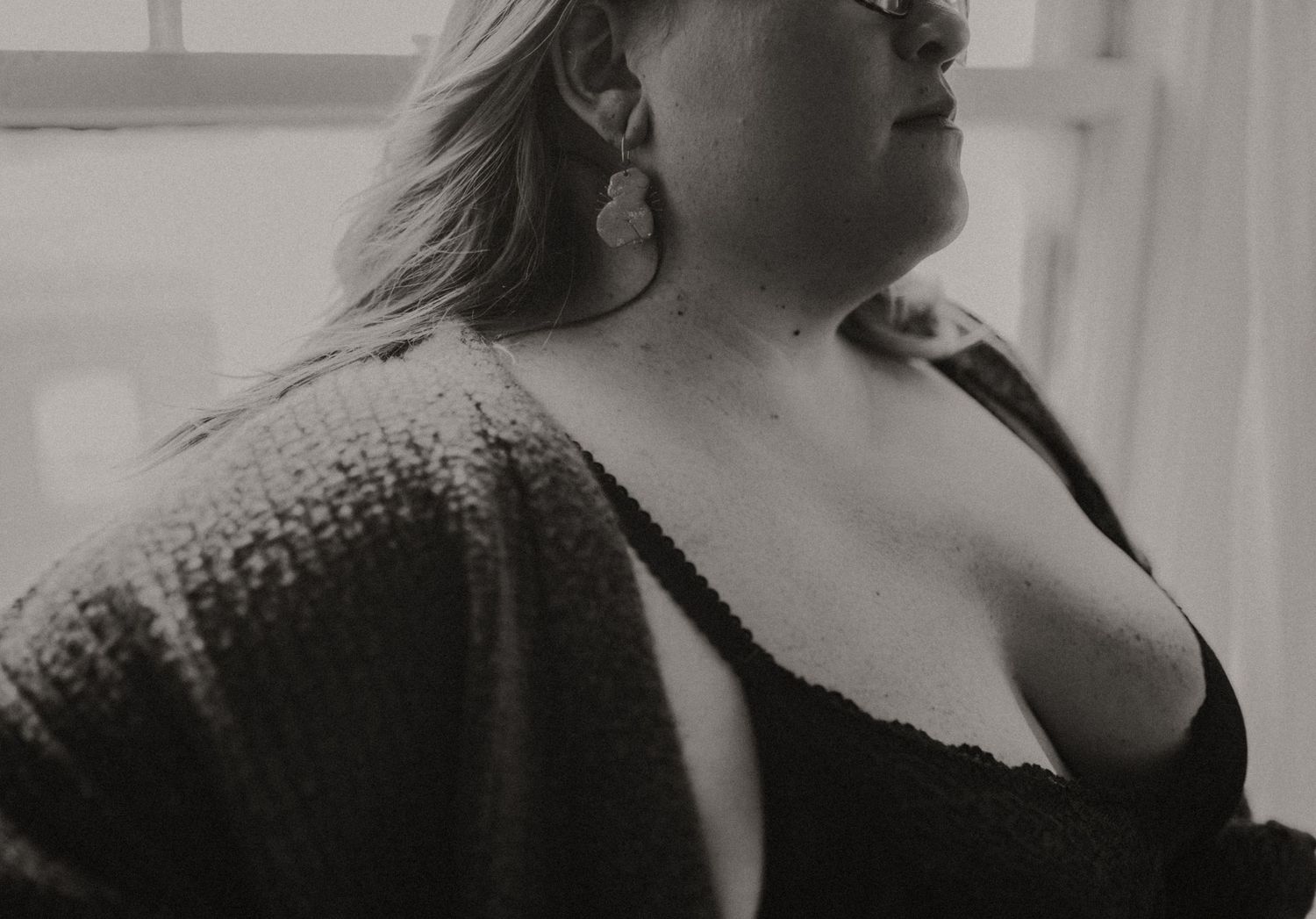 Black and white artistic boudoir photograph showing a curved silhouette of a woman wearing a chunky, textured sweater.
