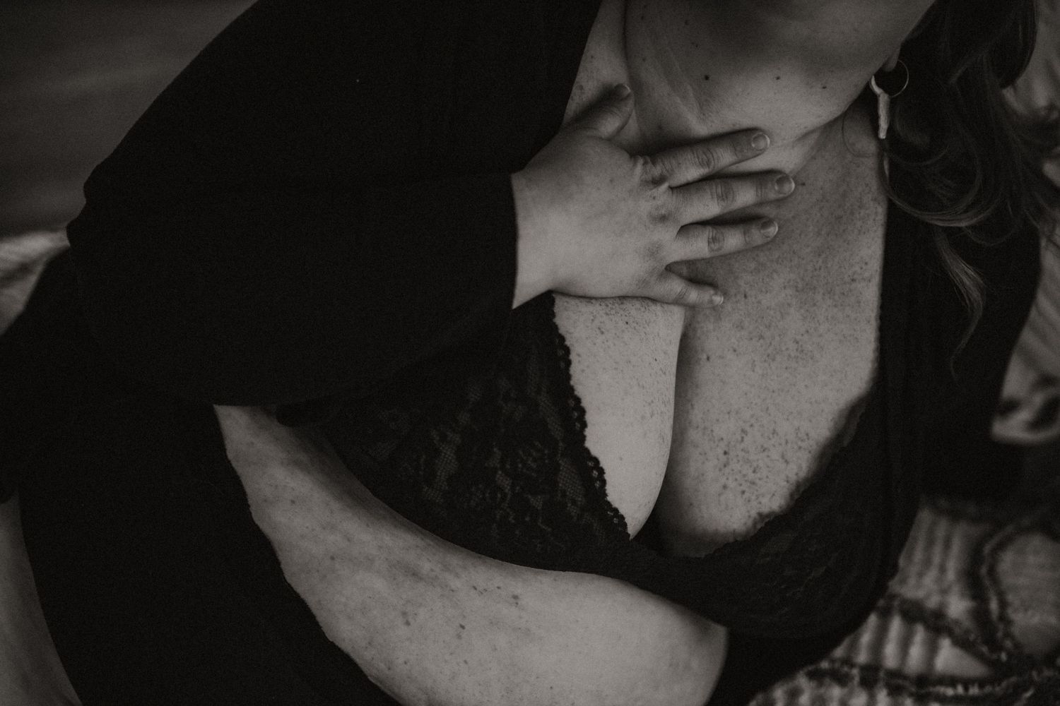 Artistic black and white close-up photograph of woman in black lace lingerie covering chest with hand.
