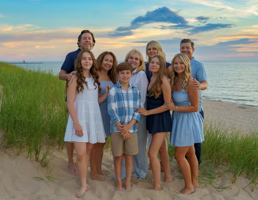 Group posing together on sandy dunes with ocean and sunset sky in background.