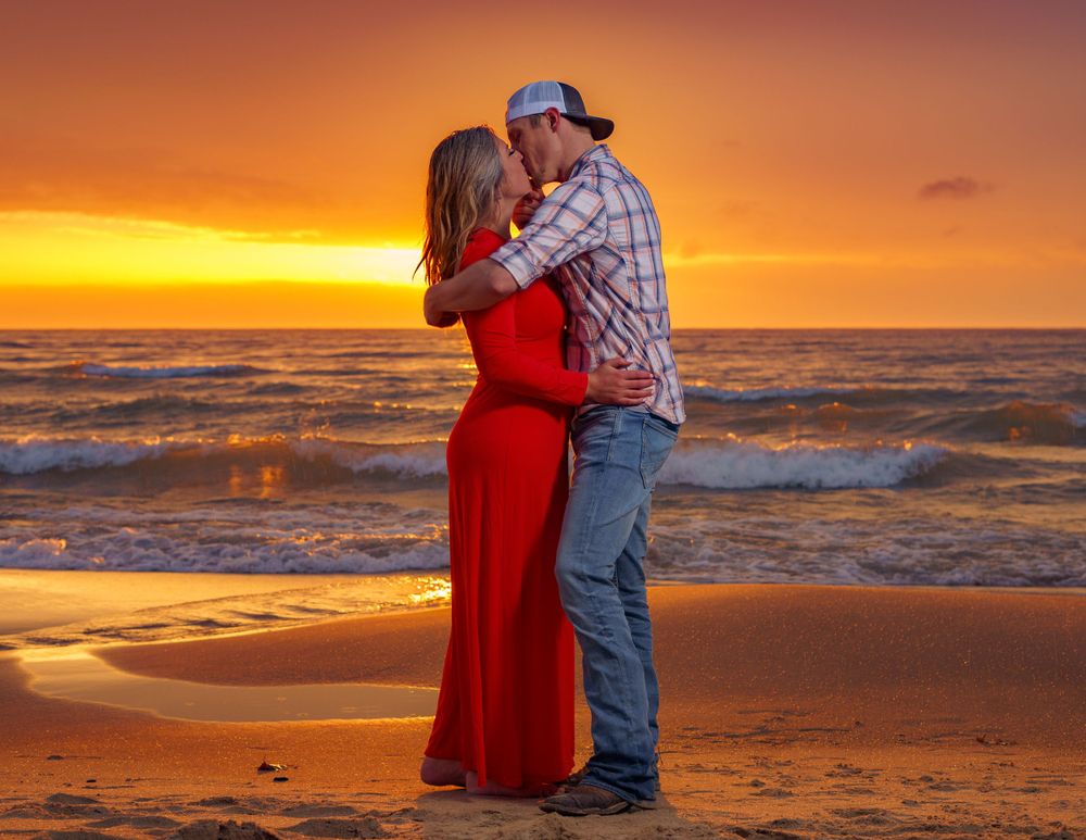 A couple embraces on a beach during a vibrant orange sunset.