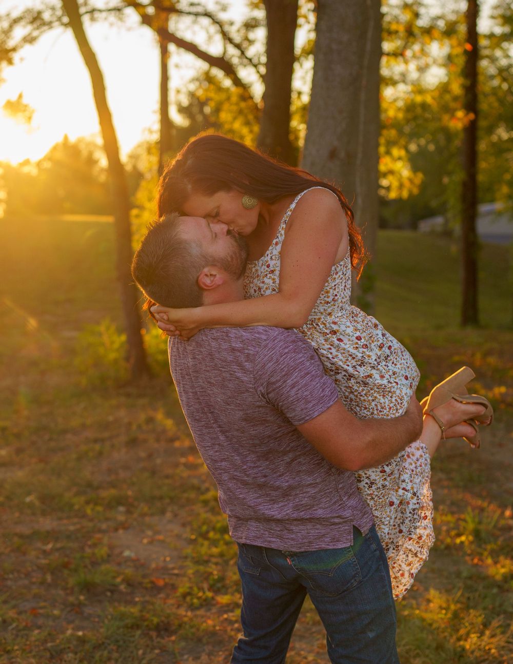 Couple embracing in passionate lift pose during golden hour in wooded setting.