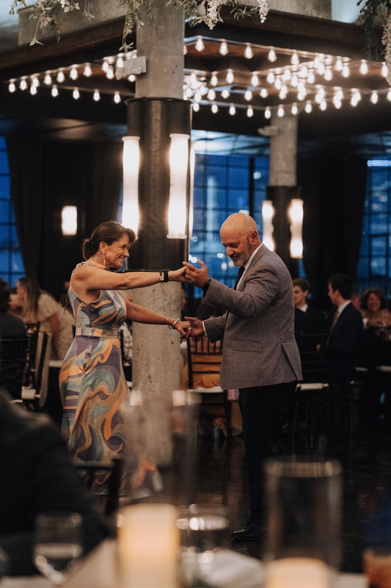 Couple dancing together under string lights at an elegant evening venue with ornate pillars and ambient lighting.