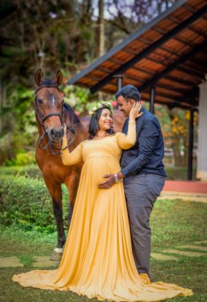 Romantic maternity photo with couple and horse, featuring flowing yellow gown in garden setting.
