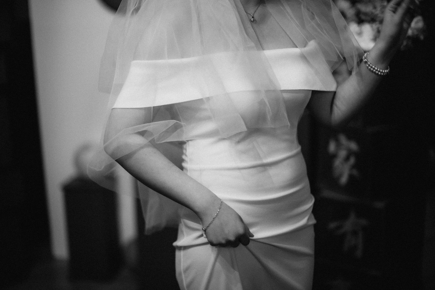Close-up black and white detail of a bride's wedding dress being adjusted.