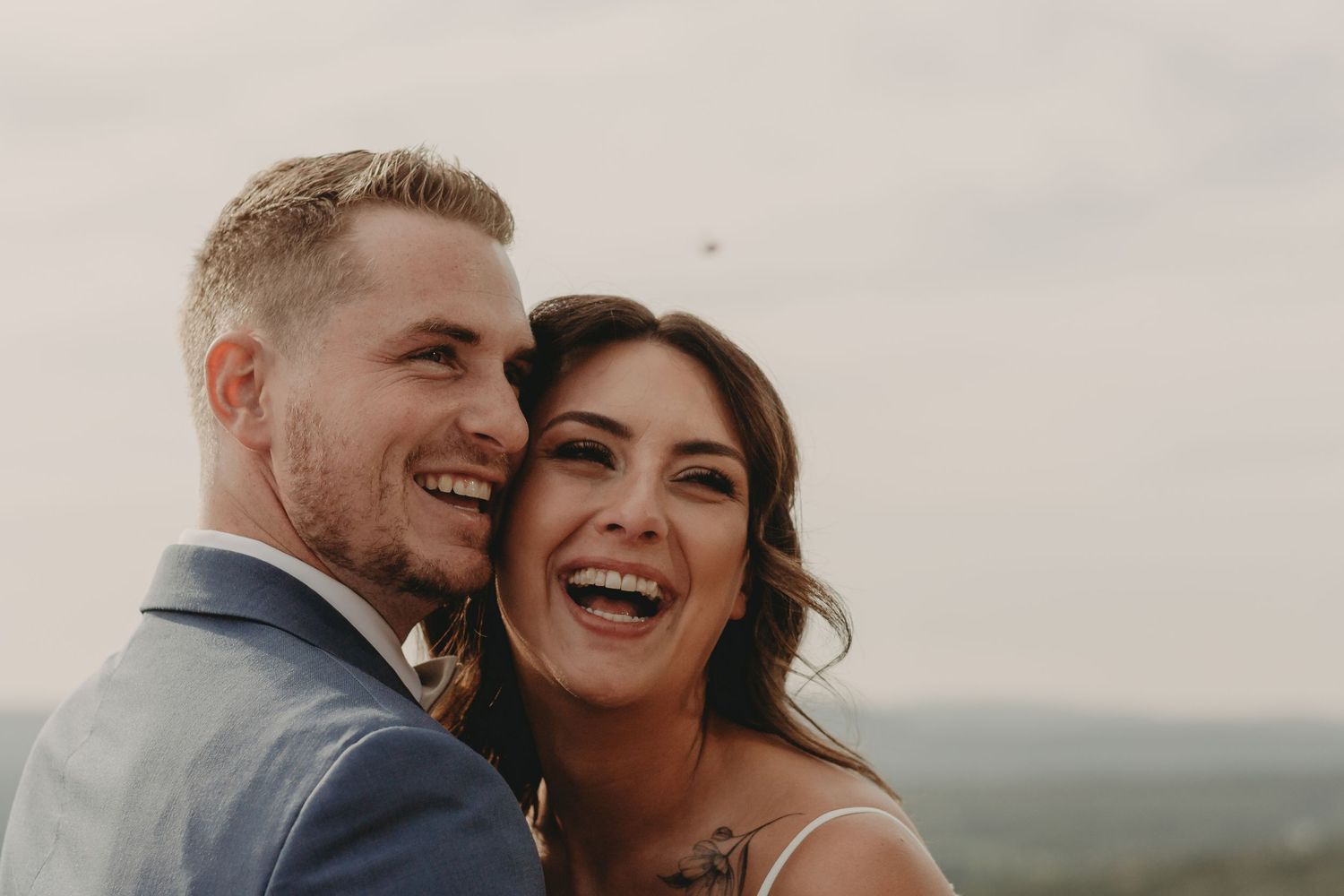 Candid outdoor wedding portrait against cloudy sky backdrop.