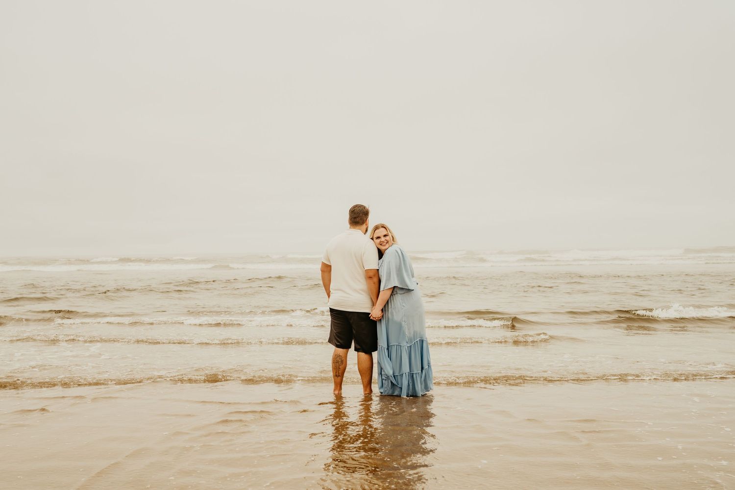 A couple standing in shallow ocean waters during a moody beach day.