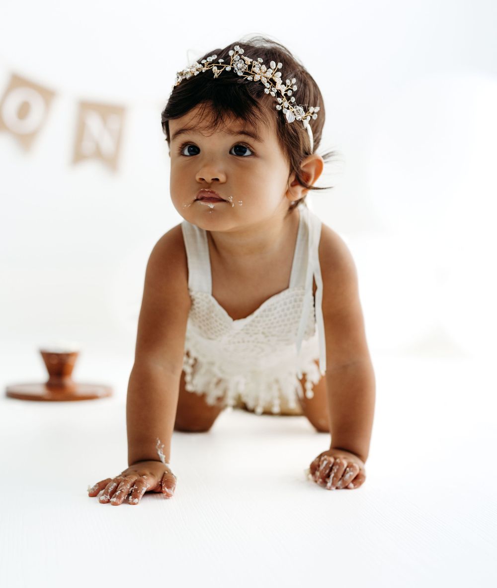 Baby in white lace outfit crawls during cake smash photo session. during a session in Fairfax, VA.