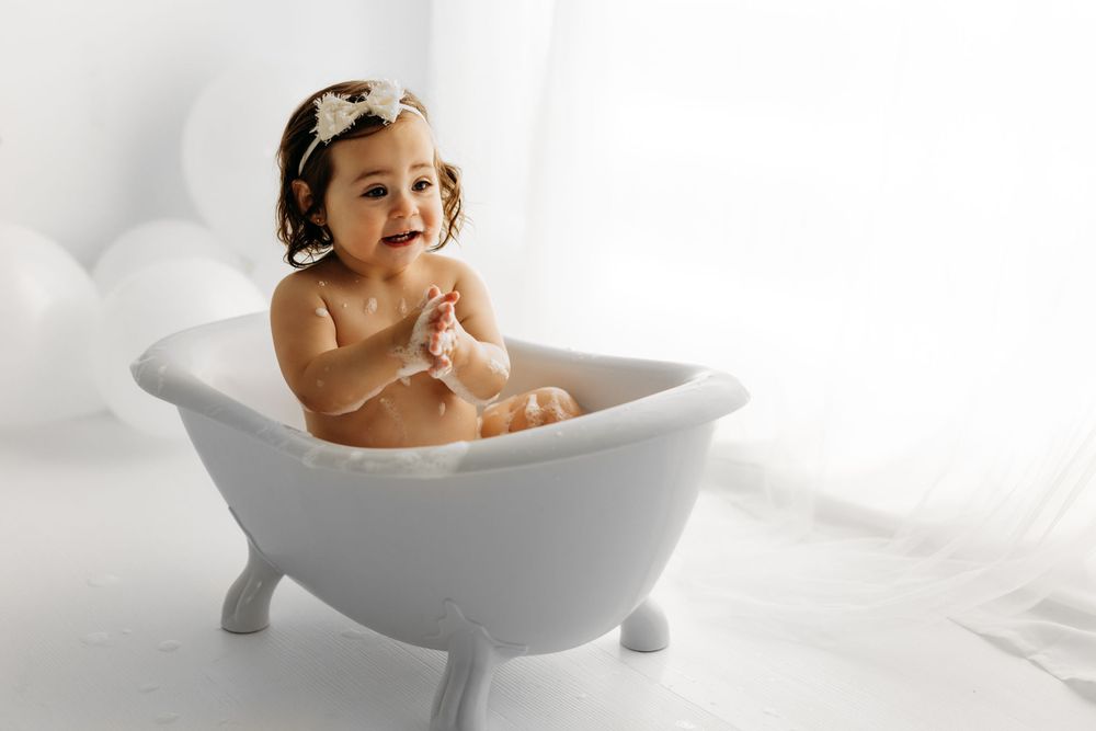 Joyful baby laughing in miniature white bathtub during photo session. during a session in Fairfax, VA.