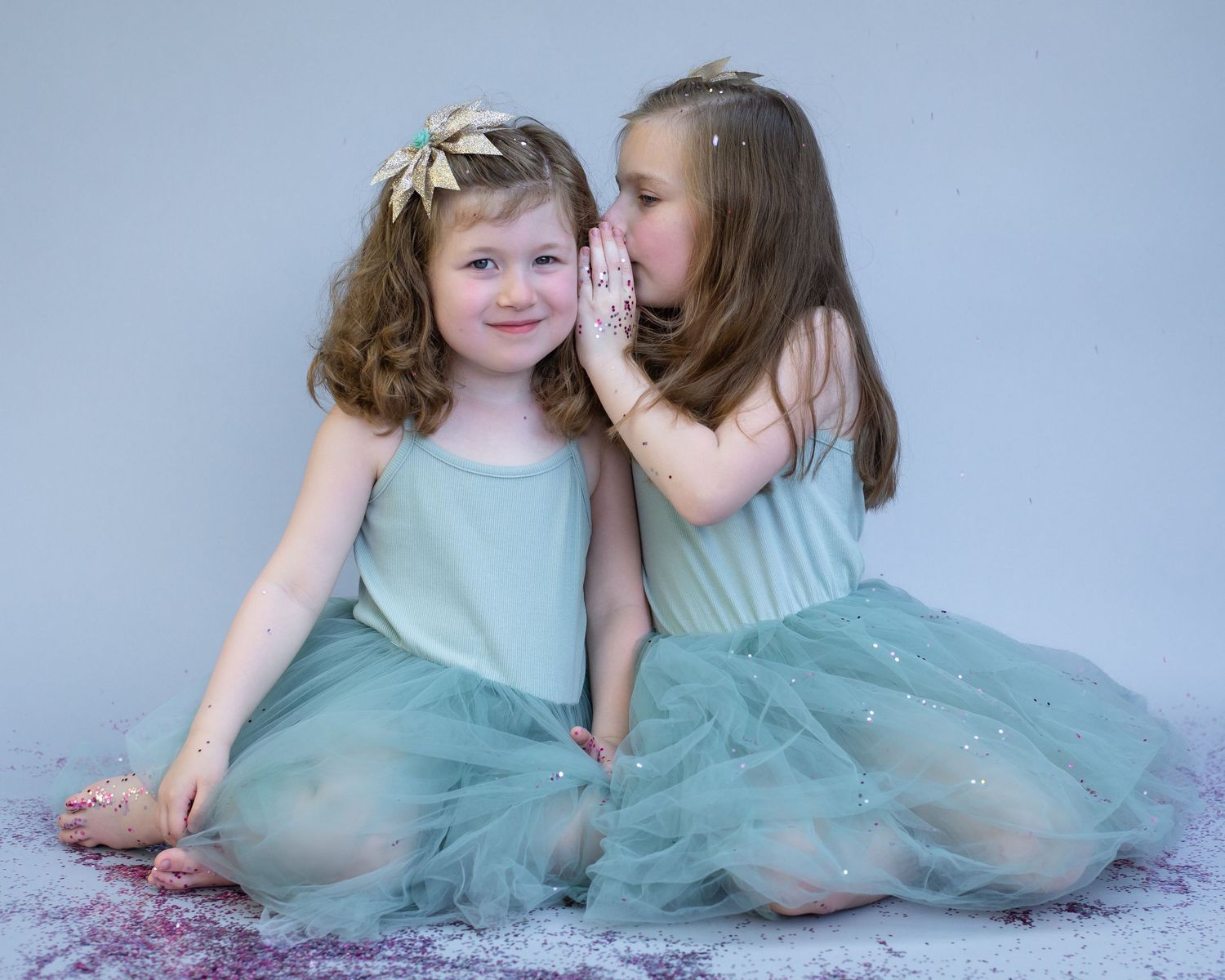 Two girls in matching mint dresses share secrets during portrait session.