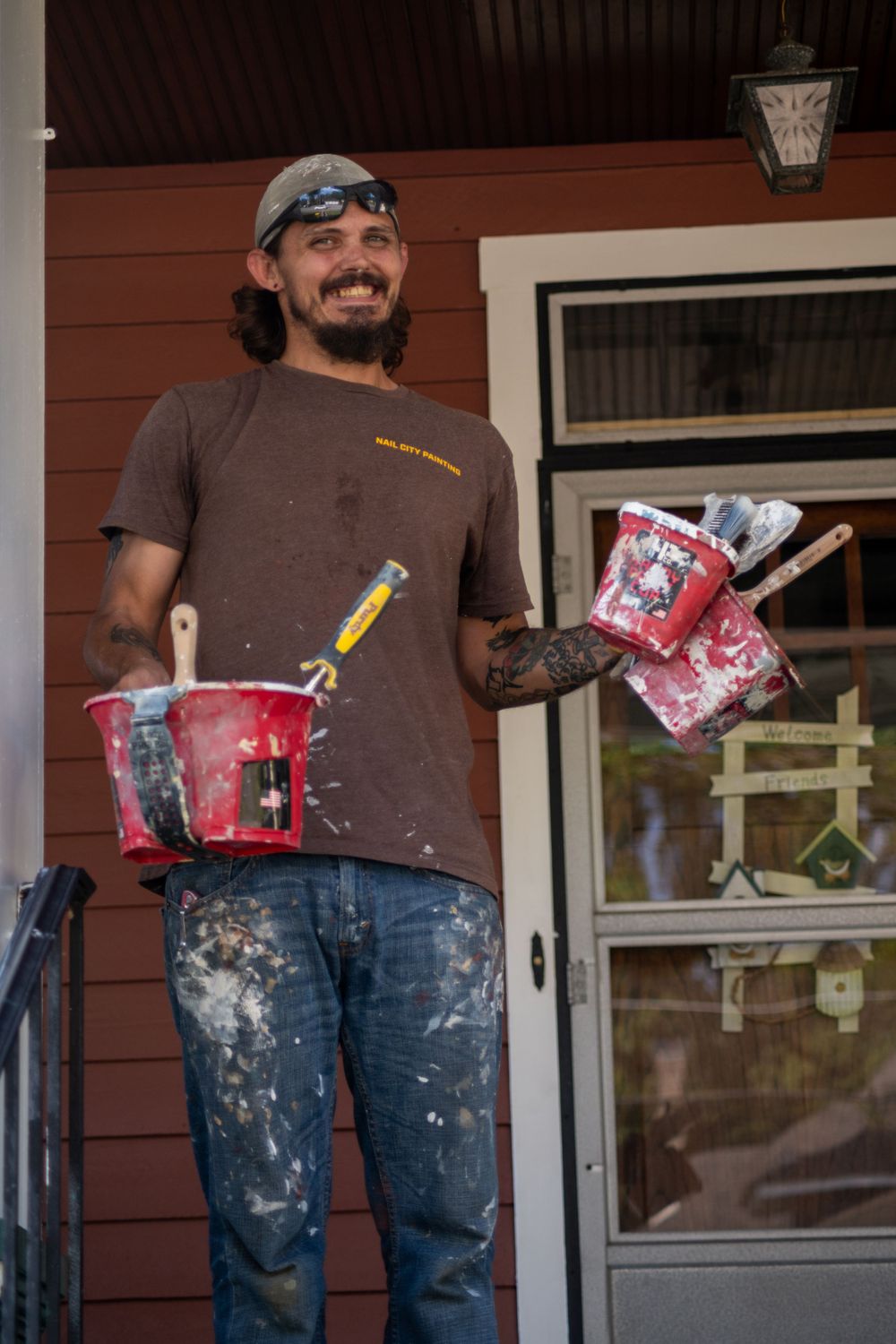 Maintenance worker holds painting supplies and tools while working on residential exterior.