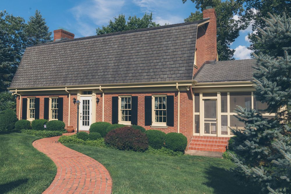 Traditional brick colonial house with curved walkway and black shutters.