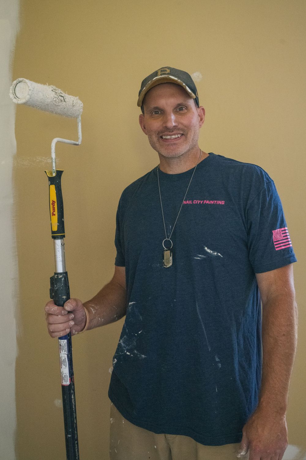 Person in navy t-shirt and baseball cap holding paint roller during home renovation project.