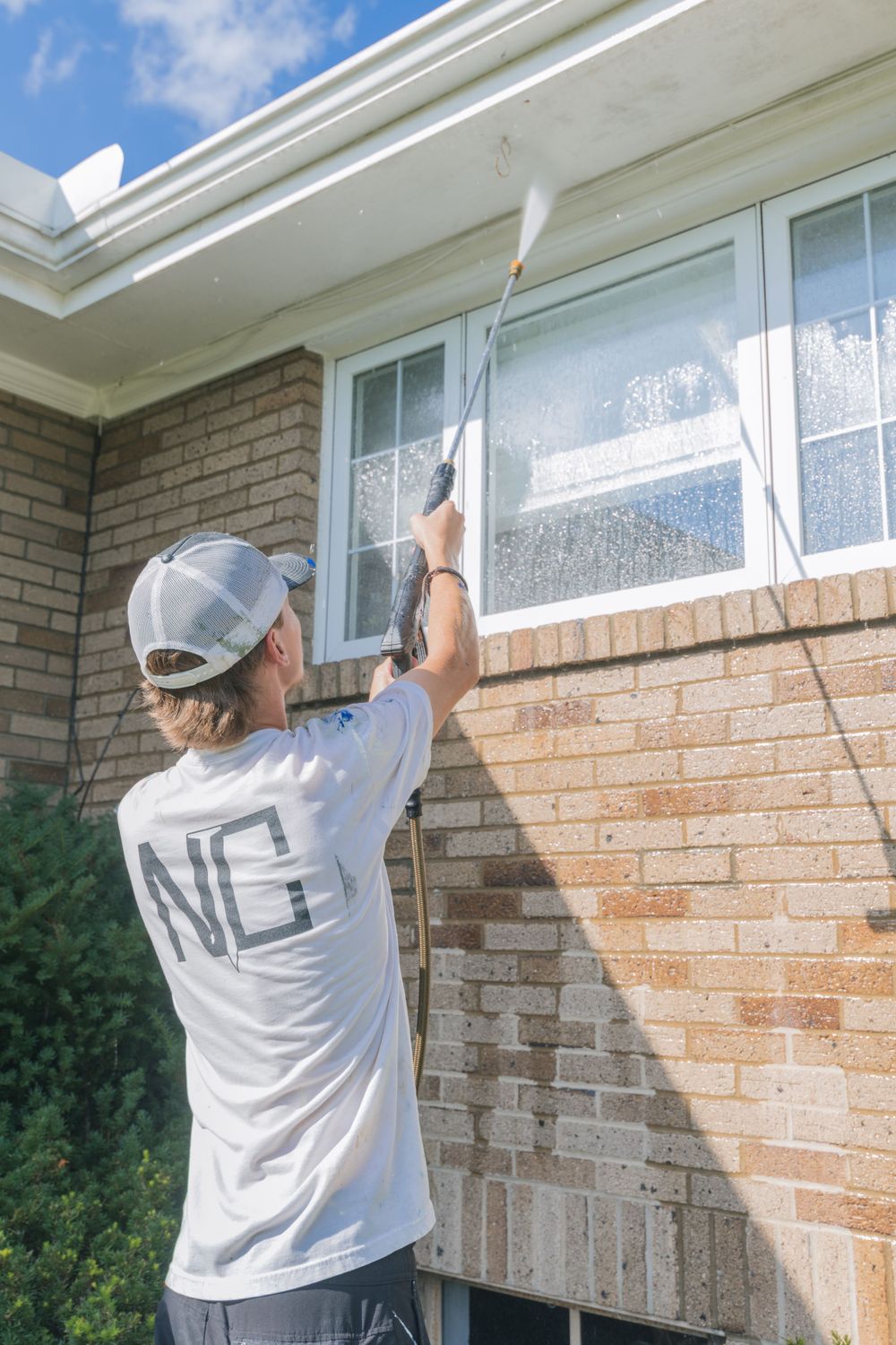 Window cleaner using extension pole to wash second story windows of brick house.