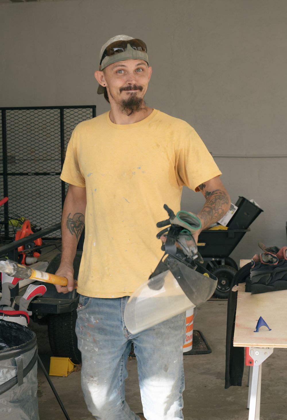 Maintenance worker in yellow t-shirt standing with tools in workshop area.