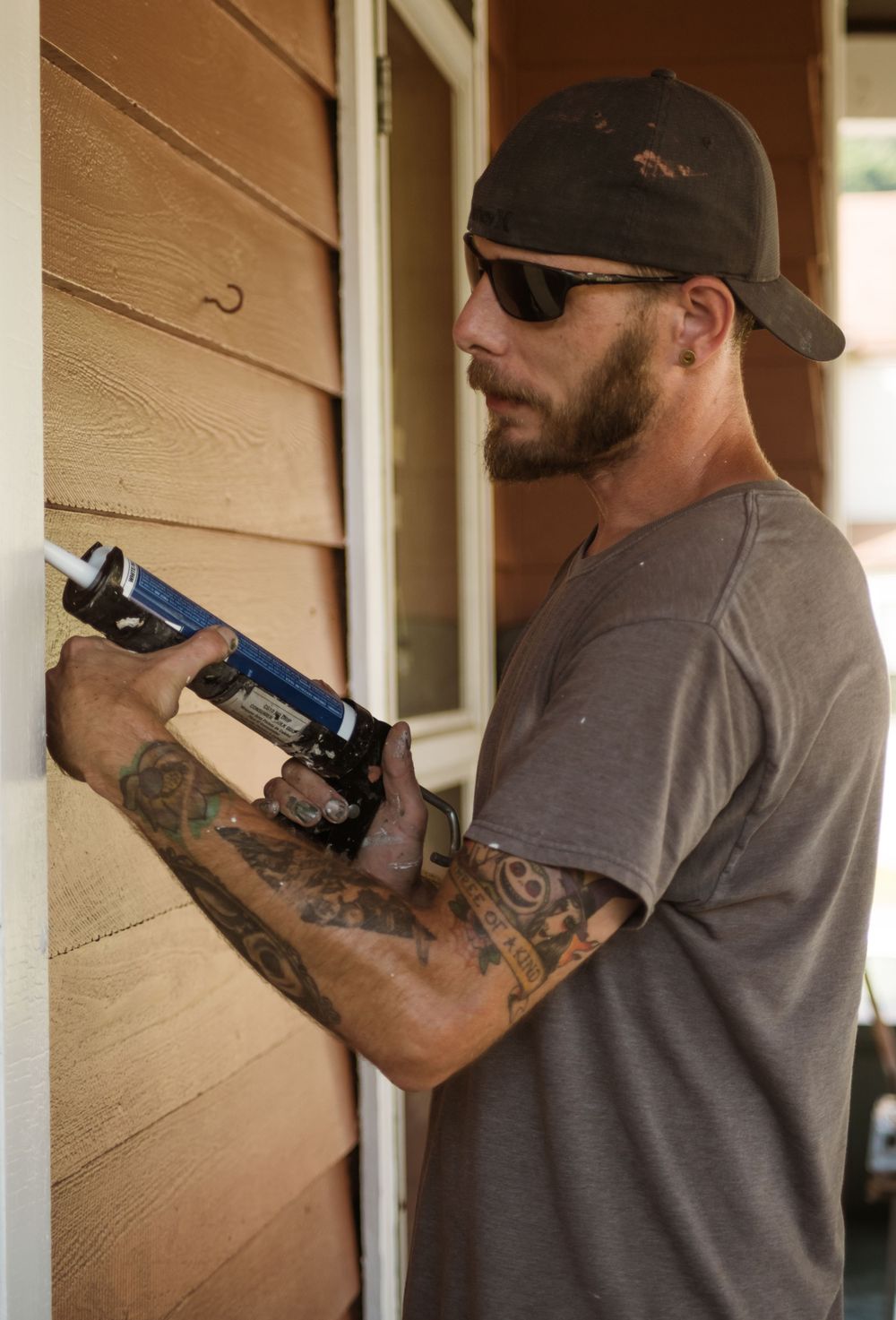 Window maintenance worker with tattoos installs new hardware while wearing protective eyewear.