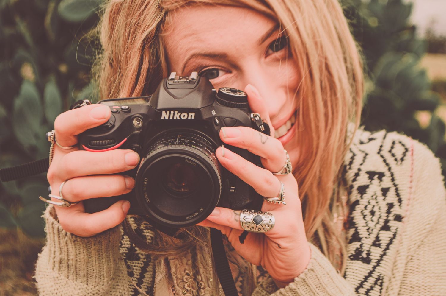 Person holding a Nikon camera while wearing a patterned sweater outdoors.