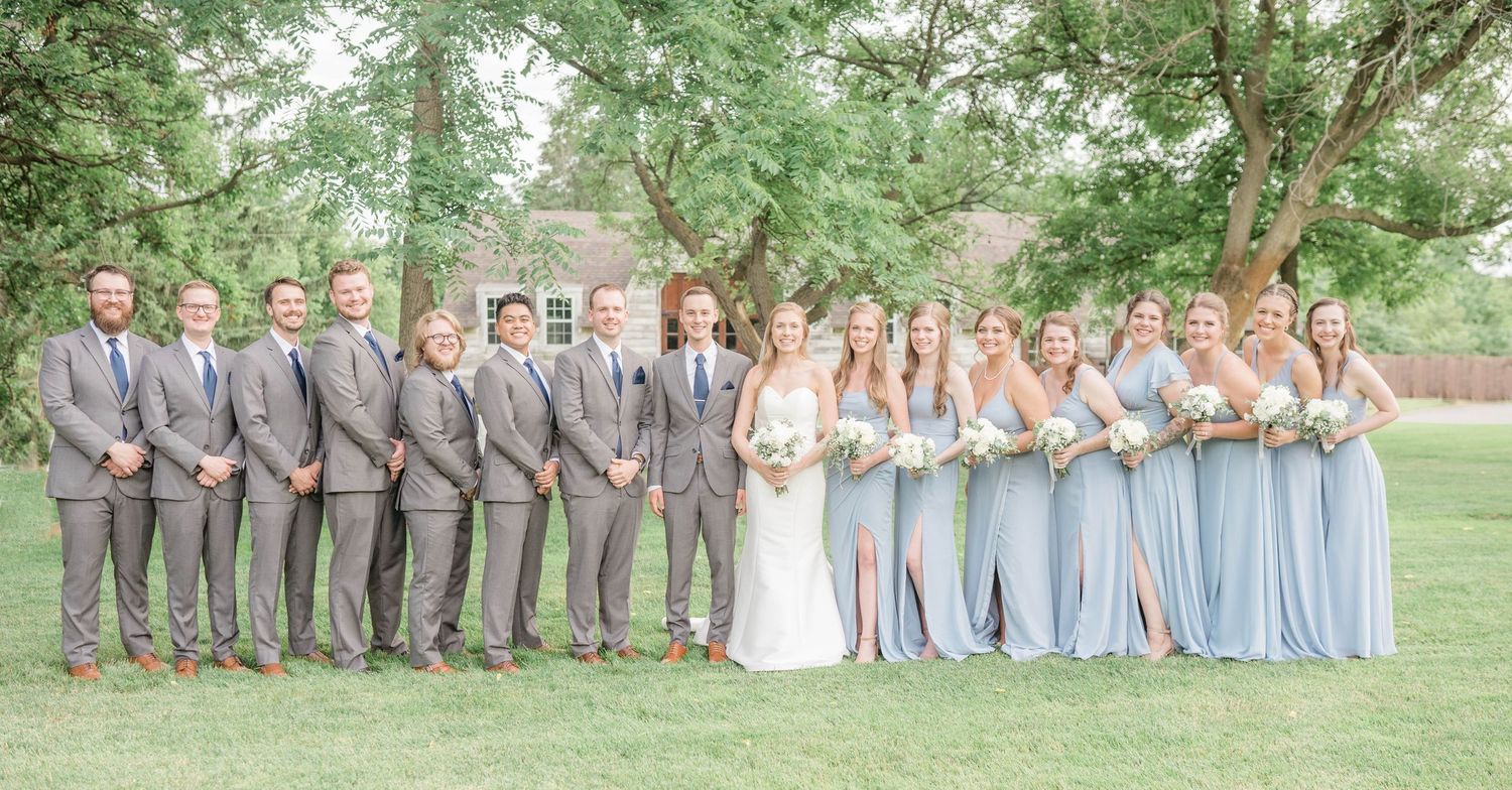 A group of people, including a bride and groom, standing together on a grassy lawn.