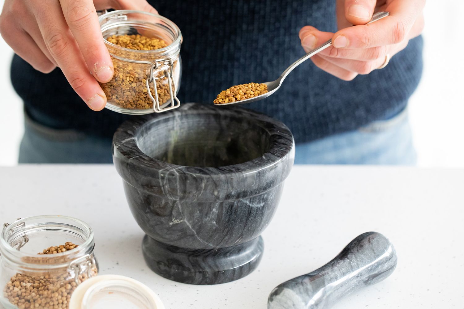 Hands measuring spices into black mortar and pestle against dark background during business branding photoshoot.