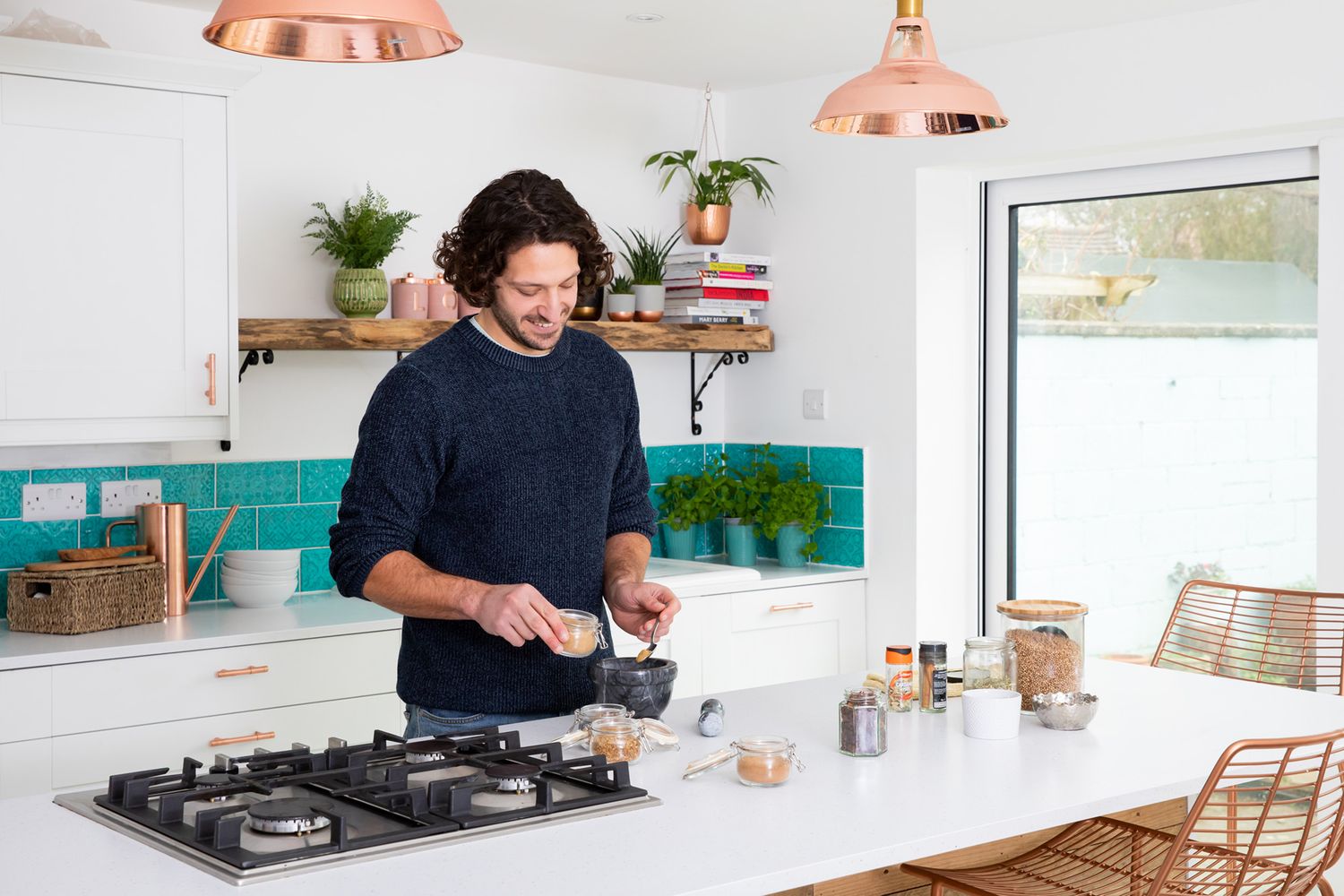 Modern bright white kitchen interior with copper pendant lights and teal backsplash tile features cook at gas stove