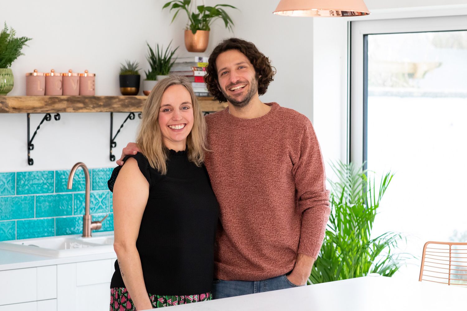 Couple standing together in modern kitchen with turquoise tile backsplash during business branding photoshoot.