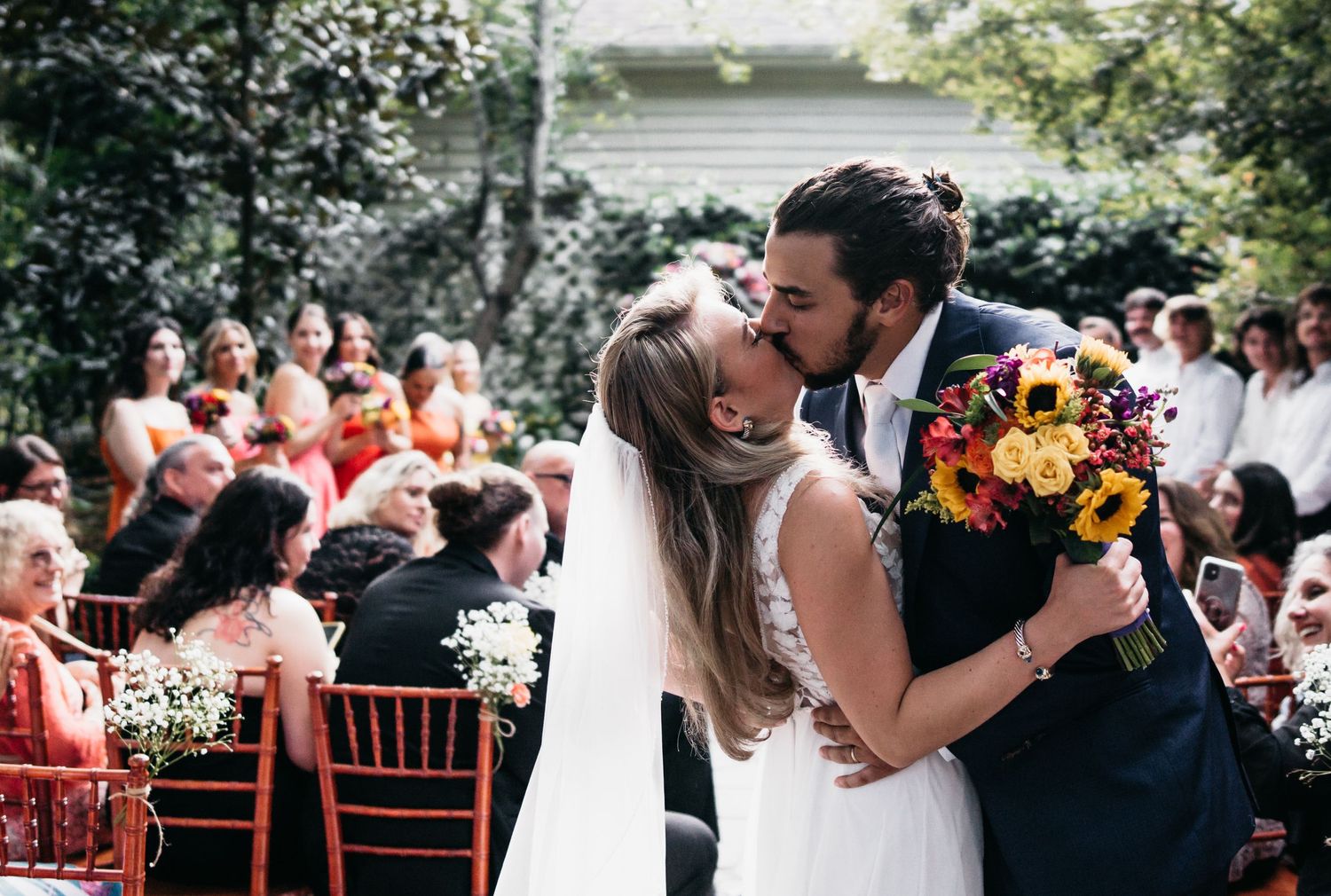 A bride in a white wedding dress is boldly kissed by a groom in the middle of the aisle after getting married